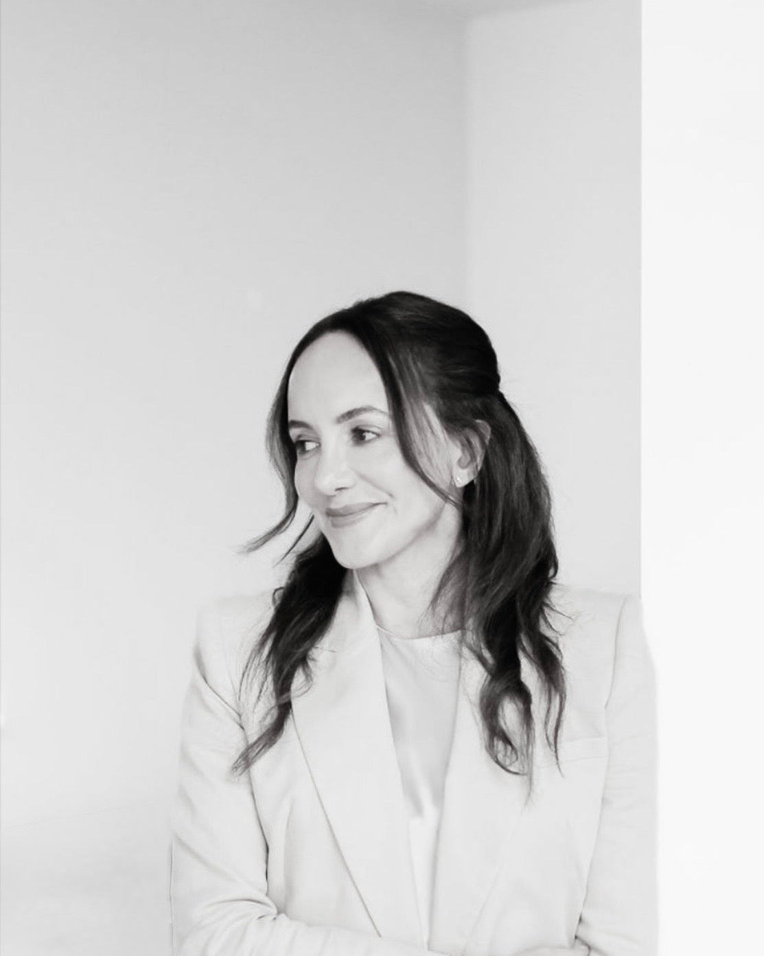 A black and white portrait of a woman with dark hair, wearing a light-colored blazer, looking to the side against a plain light background.