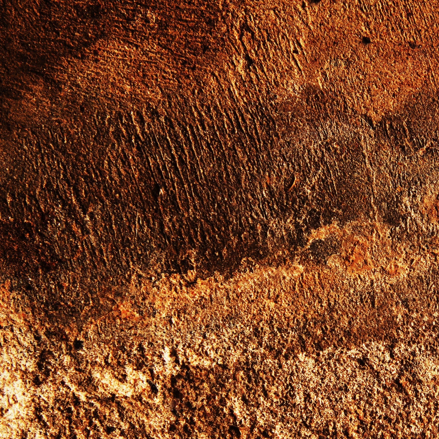 A close-up of a textured surface with a mottled pattern of earthy brown, rust orange, and dark charcoal tones.